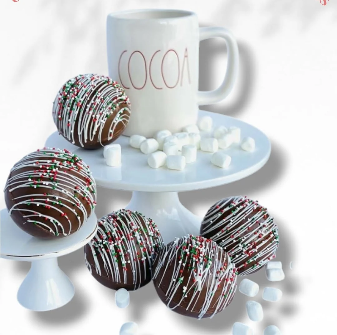 Cinco chocobombas navideñas decoradas con líneas blancas y grageas, junto a un pocillo de cocoa y malvaviscos, Detalles de Amor Medellín